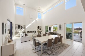 Un salón amplio con una gran mesa de comedor, chimenea y vistas al exterior.