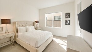 A bedroom with a large bed, bedside tables, a TV, and a window with blinds.