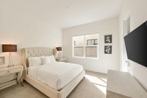 A bedroom with a large bed, bedside tables, a TV, and a window with blinds. - Palladium Palace: Pool+Spa, EV Charger, Miralon! (Palm Springs)