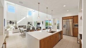 A modern kitchen with a large island, wooden cabinets, stainless steel appliances, and pendant lighting.