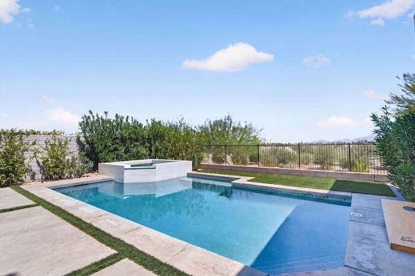 Una piscina rectangular con borde blanco, rodeada por una solana de concreto y una cerca de metal.