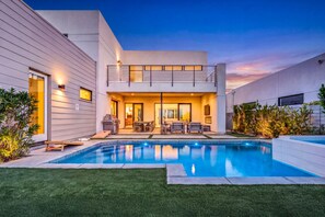 Una casa moderna de dos pisos con piscina, mobiliario exterior y un jardín bien cuidado.