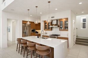 Una cocina moderna con una isla grande, taburetes de bar, electrodomésticos de acero inoxidable e iluminación colgante.