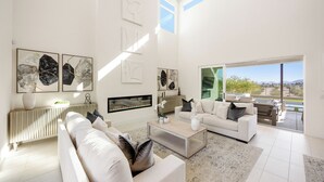 A spacious living room with a large window, a white sofa, a coffee table, and abstract art on the walls.