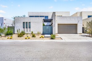 Una casa moderna de dos pisos con garaje, entrada para vehículos y un jardín delantero ajardinado con cactus.