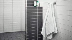 A bathroom with white and dark grey tiles, a shower area, and a towel rack with a white towel. - 1 Person Holiday Park Home in Goteborg (Gothenburg)