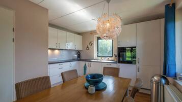 Een moderne keuken met witte kasten, een houten eettafel en een bijzondere kroonluchter.