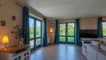 Een ruime woonkamer met een grote televisie, een bank, een houten salontafel en een lamp.