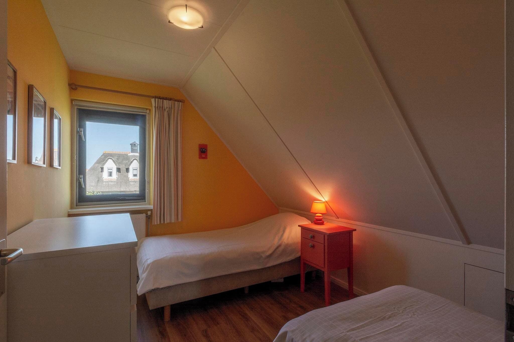 Pequeña habitación triangular con dos camas individuales, un escritorio y una ventana con cortinas.