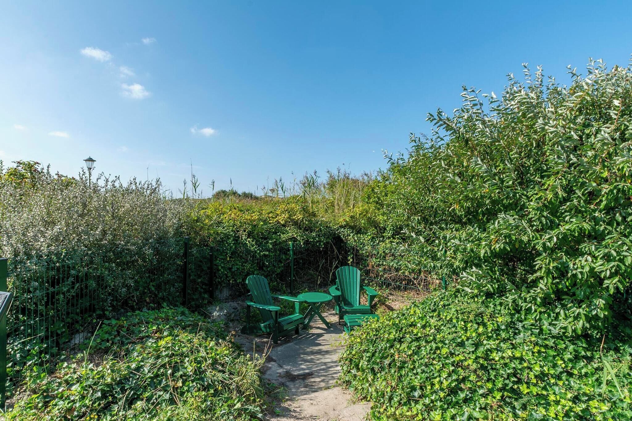 Een tuin met een geplaveid pad, groene stoelen en een tafel.