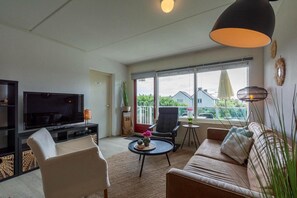 Ett vardagsrum med en TV, en soffa, stolar, ett litet bord med dekorativa föremål och stora fönster med utsikt.