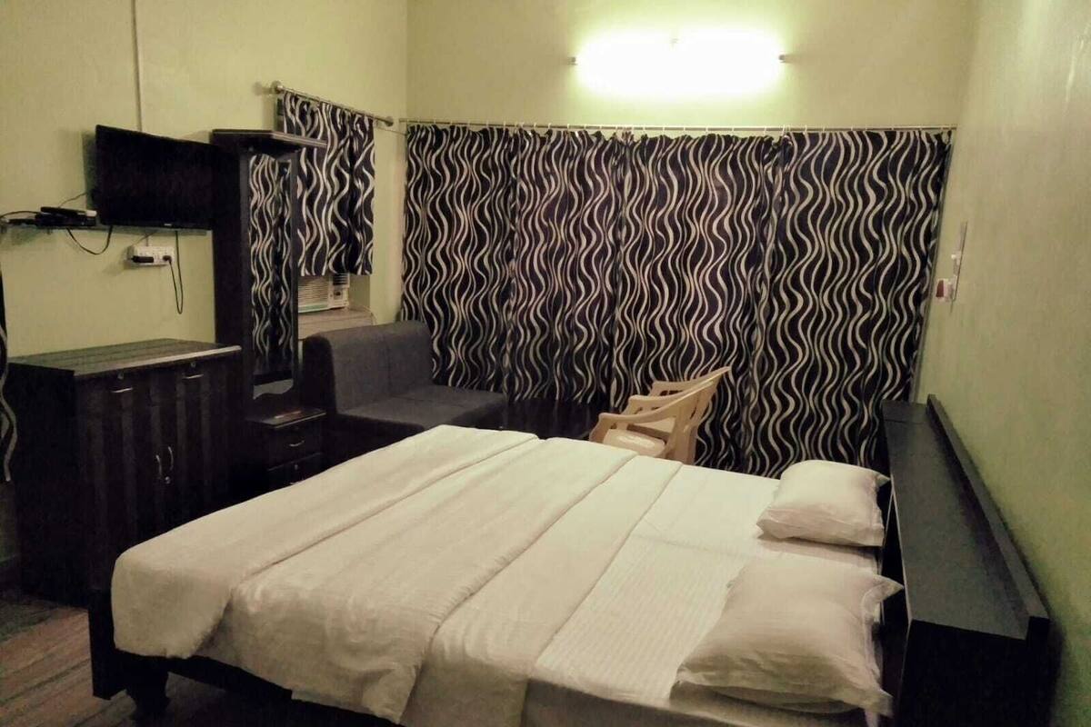 Una habitación de hotel con cama, escritorio, silla, televisor y cortina estampada.
