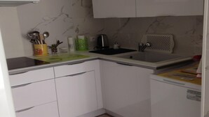 Ett kompakt kök med vita skåp, en svart kaffebryggare och en diskho.