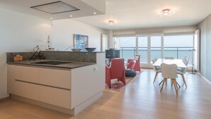Cocina moderna con una isla central, comedor con sillas rojas y un ventanal con vista al mar.