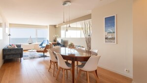 Een ruime eethoek met een houten tafel, witte stoelen, een blauwe stoel en een bank.