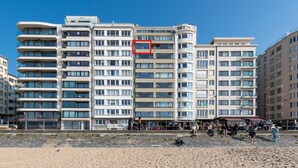 Een meerlaags hotel met balkons, een strand voorop en een helderblauwe lucht.