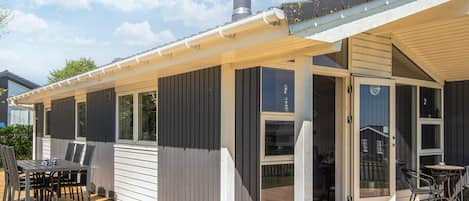 A covered outdoor area with a wooden deck, a table with chairs, and a glass door leading to an interior space.