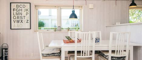 A dining area with a white table and chairs, a patterned rug, and a window with a view of greenery.