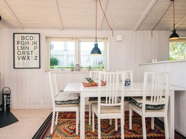 A dining area with a white table and chairs, a patterned rug, and a window with a view of greenery.