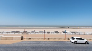 Un aparcamiento con un coche blanco, una playa al fondo y paneles solares en la playa.