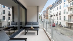 A balcony with a sofa and a table, overlooking a street with parked cars and buildings. - Apartment by the Beach in Ostend with Terrace (OSTEND)
