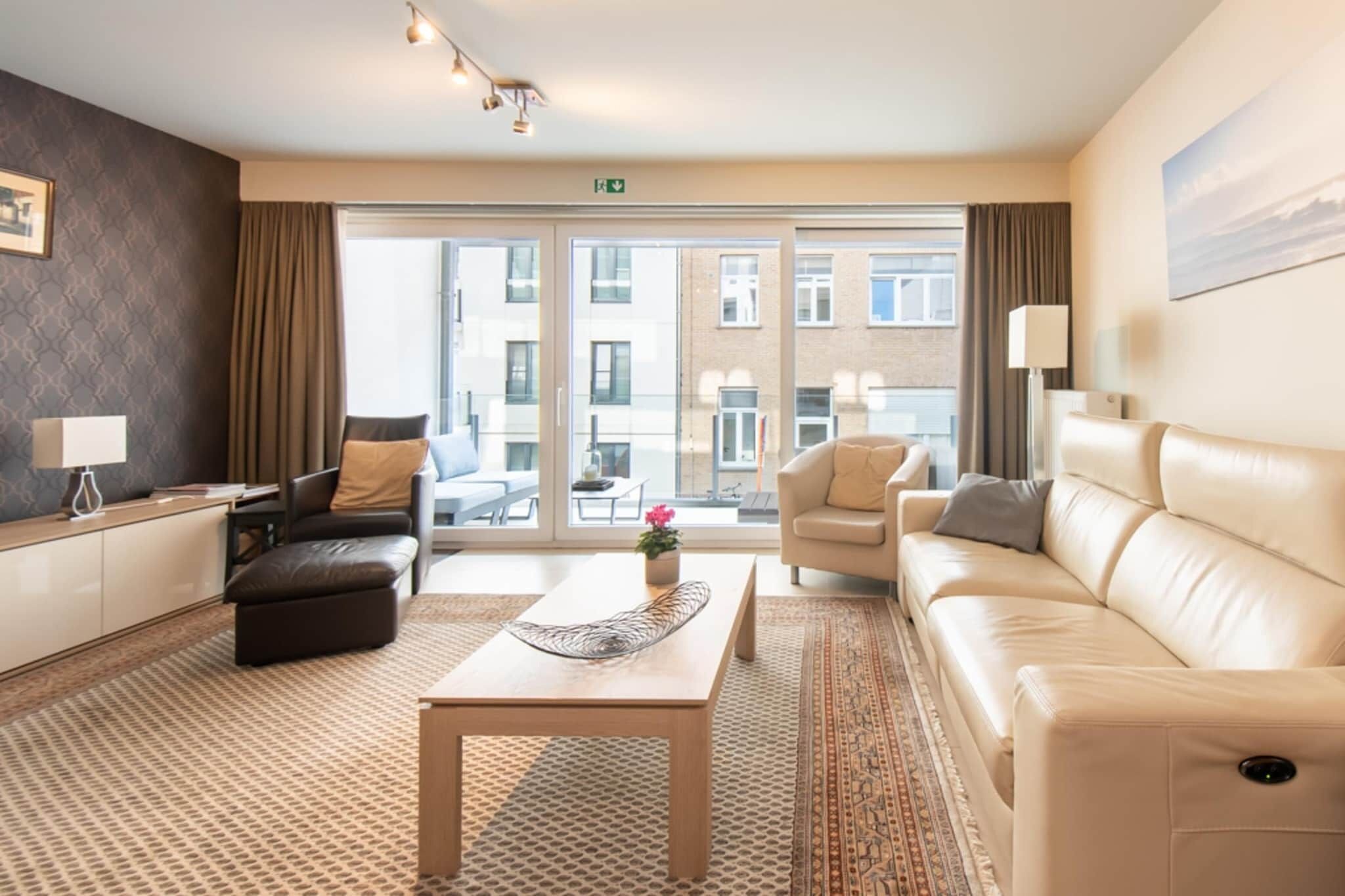 A modern hotel room with a large window, a sofa, a chair, a coffee table, and a small table with a lamp.