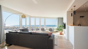 Una sala moderna con un sofá gris grande, una lámpara de pie y vista al mar.