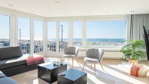 Un salón espacioso con un ventanal que ofrece vistas a la playa y al paisaje urbano.