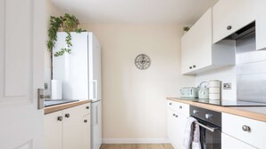 A modern kitchen with white cabinets, a wooden countertop, a built-in oven, and a clock on the wall.