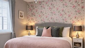 A bedroom with a large bed, floral wallpaper, a chandelier, and two bedside tables with lamps.
