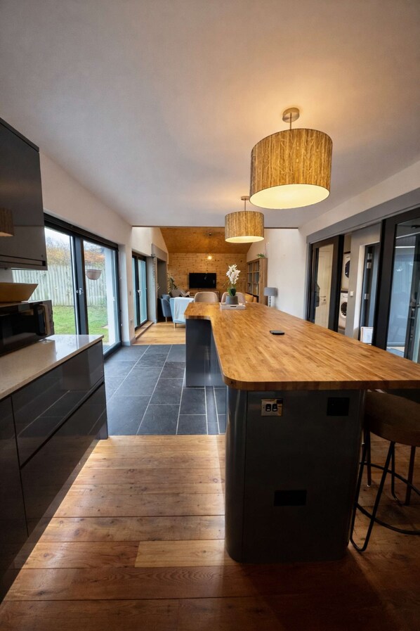 A modern kitchen with a wooden island, dark cabinetry, and a large window. - The Highland Moonray (Inverness)