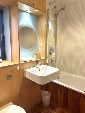 Un baño con tocador de madera, lavamanos, espejo, cabina de ducha e inodoro.