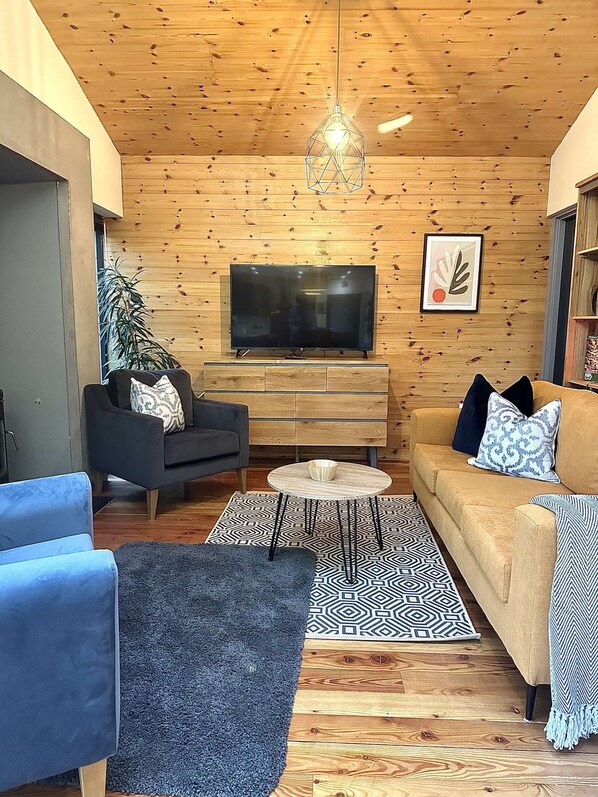 Una sala de estar acogedora con techo de madera, un televisor de pantalla plana, un sofá, una mesa de centro y un tapete estampado.