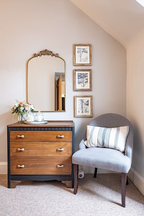 Classic elegance defines this well-appointed room, featuring a dresser, mirror, and botanical prints.