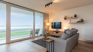A modern living room with a large window, a grey sofa, a flat-screen TV, and a small table.