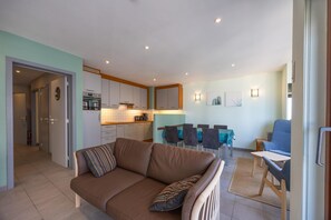 A living room with a brown sofa, a dining area with a table and chairs, and a kitchen with cabinets and appliances. - Apartment in Ostend near the beach (OSTEND)