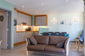 Un espacio habitable compacto con kitchenette, un sofá, una mesa de comedor con sillas y obras de arte en las paredes.