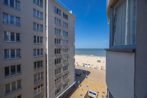 A high-rise building with multiple windows and balconies overlooking a beach.
