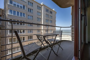 A balcony with a table and chairs, overlooking a building and a beach.