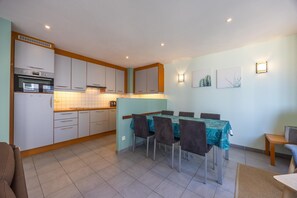 Cocina compacta con zona de comedor, que incluye una mesa con sillas, horno integrado y salpicadero de azulejos.