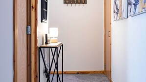 Un couloir avec une porte en bois, une petite table avec une lampe et des œuvres d’art abstrait accrochées aux murs.