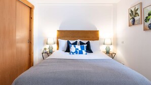 Une chambre d’hôtel avec un grand lit, deux tables de chevet avec des lampes, une armoire en bois et deux tableaux encadrés au mur.