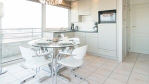 Een moderne keuken met witte kasten, een roestvrijstalen koelkast en een eethoek met een glazen tafel en witte stoelen.