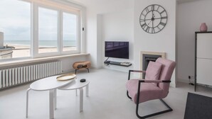 Ein modernes Wohnzimmer mit großem Fenster, Flachbildfernseher, Kamin und einer Wanduhr.