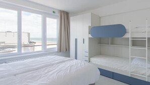 Ein modernes Hotelzimmer mit einem großen Bett, einem Etagenbett und Blick auf den Strand.