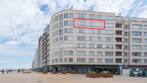 Ein mehrstöckiges Hotel mit geschwungener Fassade, Außenbereichen zum Sitzen und einem wolkenlosen Himmel.