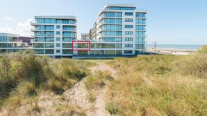A modern building with multiple floors and large windows, situated near a beach with a clear sky. - Apartment in Oostende near Beach & Dunes (OSTEND)