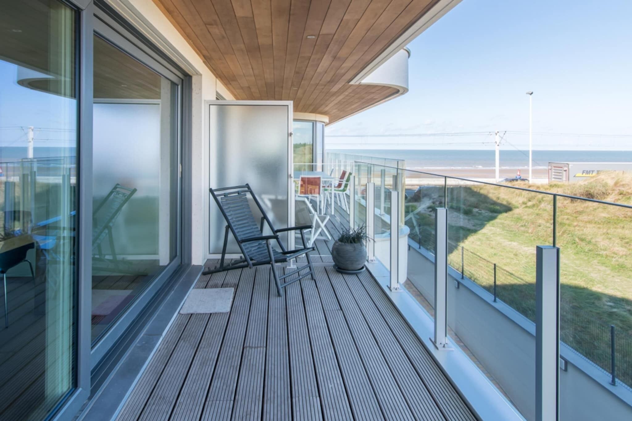 A balcony with a wooden deck, glass doors, and a view of the beach.