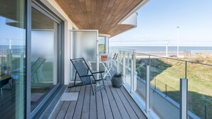 A balcony with a wooden deck, glass doors, and a view of the beach. - Apartment in Oostende near Beach & Dunes (OSTEND)