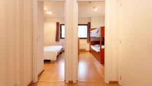 Ein Zimmer mit Holzboden, einem Etagenbett, einem Einzelbett und einem Fenster mit Vorhängen.